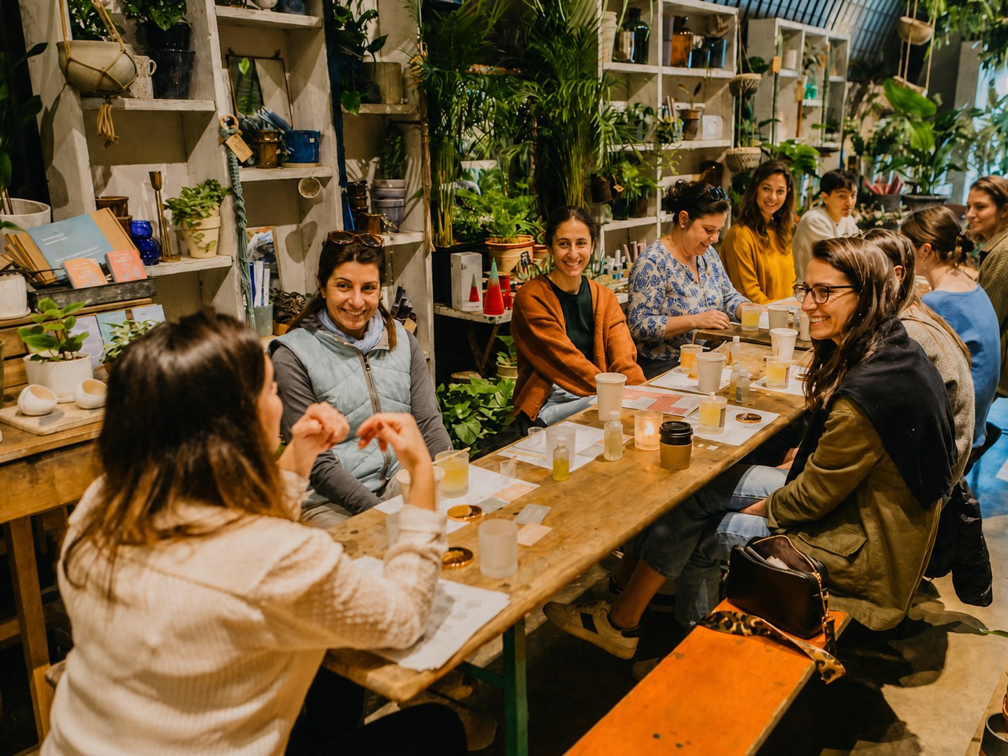 Smiling guests gathered around a plant-filled candle workshop table